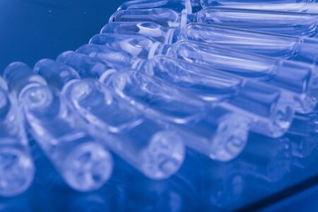 Glass medical ampoule vial for injection. Medicine is liquid sodium chloride with of aqueous solution in ampulla. Close up. Bottles ampule multicolor on background color and water. Human plasma.の写真素材