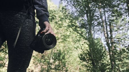 Traveler photographing scenic view in forest. One caucasian woman shooting close up look. Girl hold dslr mirrorless camera in his hand. Professional photographer travel with backpack. Outdoor.の写真素材