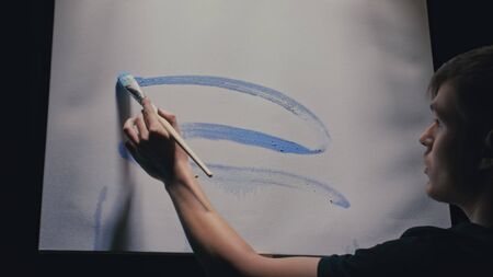 Artist copyist paint seascape with ship in ocean. Craftsman decorator draw as boat sail on blue sea with acrylic oil color. Draw finger, brush, knife palette. Indoor. Dark magic cinematic look.の写真素材