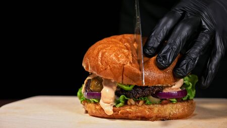 Cut craft burger is cooking on black background. Consist: red sauce salsa, lettuce, red onion, pickle, cheese, chilli green pepper, air bun and marbled meat beef. Not made ideal. Loving hand made.の写真素材