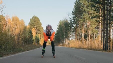 Training an athlete on the roller skaters. Biathlon ride on the roller skis with ski poles, in the helmet. Autumn workout. Roller sport. Adult man riding on skates.の写真素材