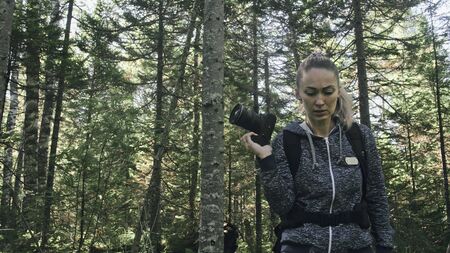 Traveler photographing scenic view in forest. One caucasian woman shooting nice magic look. Girl take photo video on dslr mirrorless camera. Professional photographer travel with backpack. Outdoor.の写真素材