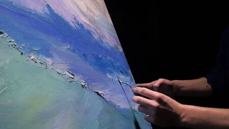 Artist copyist paint seascape with ship in ocean. Craftsman decorator draw as boat sail on blue sea with acrylic oil color. Draw finger, brush, knife palette. Indoor. Dark magic cinematic look.の写真素材