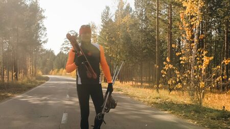 Training an athlete on the roller skaters. Biathlon ride on the roller skis with ski poles, in the helmet. Autumn workout. Roller sport. Adult man riding on skates. Athlete is getting ready to start.の写真素材