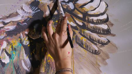 Artist designer draws an eagle on the wall. Craftsman decorator paints a picture with acrylic oil color brush. Close-up dark magic cinematic look. Painter dressed in a paint coat. Indoor.の写真素材