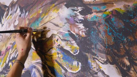 Artist designer draws an eagle on the wall. Craftsman decorator paints a picture with acrylic oil color brush. Close-up dark magic cinematic look. Painter dressed in a paint coat. Indoor.の写真素材