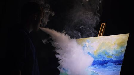 Artist copyist paint seascape with ship in ocean. Vaper smoke vape e-cigarette. Craftsman decorator draw as boat sail on blue sea with acrylic oil color. Draw finger, brush, knife palette. Indoor.の写真素材