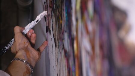 Artist designer draws an eagle on the wall. Craftsman decorator paints a picture with acrylic oil color brush. Close-up dark magic cinematic look. Painter dressed in a paint coat. Indoor.の写真素材