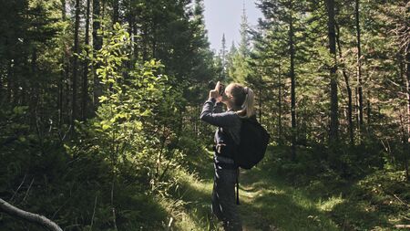 Traveler photographing scenic view in forest. One caucasian woman shooting nice magic look. Girl take photo video on dslr mirrorless camera. Professional photographer travel with backpack. Outdoor.の写真素材