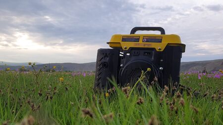 Close up of gas diesel mobile portable electricity generator work on grass. Gasoline fuel powered portable generator give electric energy current for camping. Background: grass, tent, car. Outdoor.の写真素材