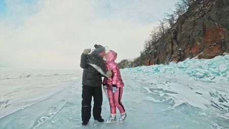 Couple has fun winter walk against background of ice of frozen lake. Lovers lie on clear ice with cracks have fun kiss and hug. View from above. Happy people on snow covered ice. Honeymoon love story.の写真素材