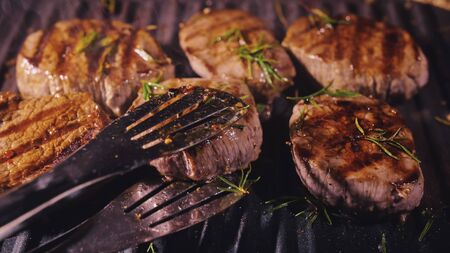 Delicious juicy meat steak cooking on grill. Kitchen tongs. Aged prime rare roast grilling...