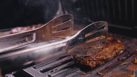 Delicious juicy meat steak cooking on grill. Kitchen tongs. Aged prime rare roast grilling tenderloin fresh marble tenderness beef. Prime beef fry on electric roaster, rosemary black pepper, salt.の写真素材