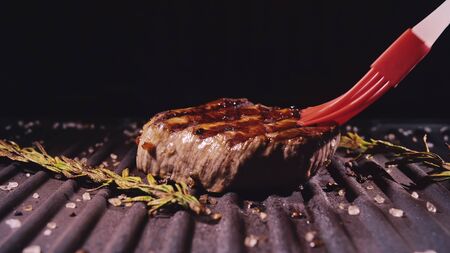 Delicious juicy meat steak cooking on grill. Silicone cooking brush. Aged prime rare roast grilling fresh marble tenderness beef. Prime beef fry on electric roaster, rosemary black pepper oil.の写真素材