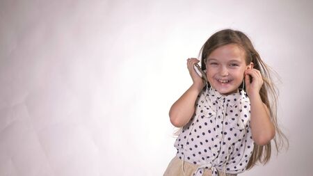 Child with earflaps dancing at studio background. The girl listens to music on the smartphone. The kid has loose long hair. Beautiful cute happy little girl listens to music on Headphones.の写真素材