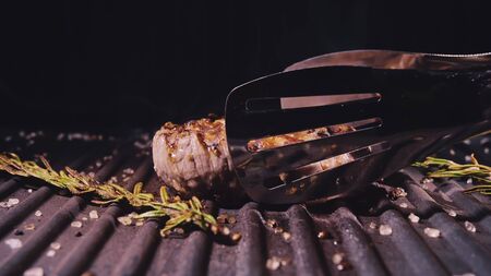 Delicious juicy meat steak cooking on grill. Kitchen tongs. Aged prime rare roast grilling tenderloin fresh marble tenderness beef. Prime beef fry on electric roaster, rosemary black pepper, salt.の写真素材
