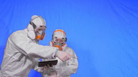 Scientist virologist in respirator makes write in an tablet computer with stylus. Man and woman wearing protective medical mask. Health safety virus coronavirus epidemic 2019 nCoV. Chroma key blue.の写真素材