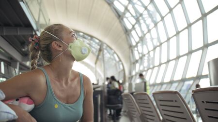 Woman caucasian at airport with wearing protective medical mask on head against the background of the plane. Concept health safety virus protection coronavirus epidemic sars-cov-2 covid-19 2019-ncov.の写真素材