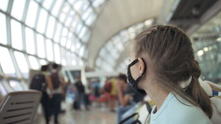 Children girl kid caucasian at airport with wearing protective medical mask on head against background of plane. Concept health virus protection coronavirus epidemic sars-cov-2 covid-19 2019-ncov.の写真素材