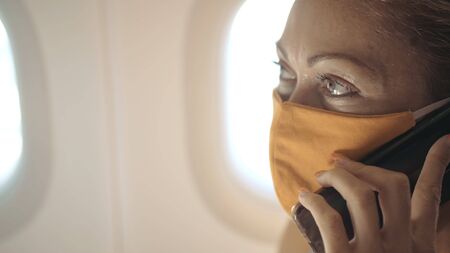 Woman travel tourist caucasian at plane aircraft with wearing protective medical mask. Girl talking about coronovirus on phone smartphone mobile. Virus epidemic sars-cov-2 covid-19 2019-ncov.の写真素材