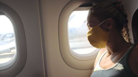 Woman travel caucasian at plane with wearing protective medical mask. Girl tourist at aircraft with protect respirator. Concept virus protection coronavirus epidemic sars-cov-2 covid-19 2019-ncov.の写真素材