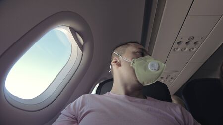 Man travel caucasian at plane with wearing protective medical mask. Male tourist at aircraft with protect respirator. Concept virus protection coronavirus pandemic sars-cov-2 covid-19 2019-ncov.の写真素材