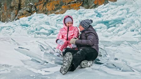 Couple has fun winter walk against background of ice of frozen lake. Lovers lie on clear ice with cracks have fun kiss and hug. View from above. Happy people on snow covered ice. Honeymoon love story.の写真素材