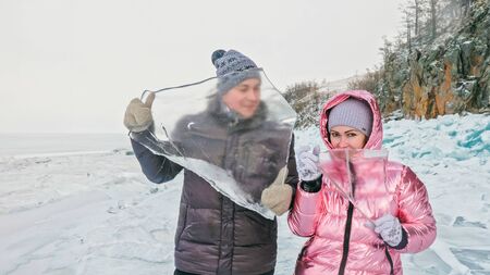 Couple has fun winter walk against background of ice of frozen lake. Lovers lie on clear ice with...