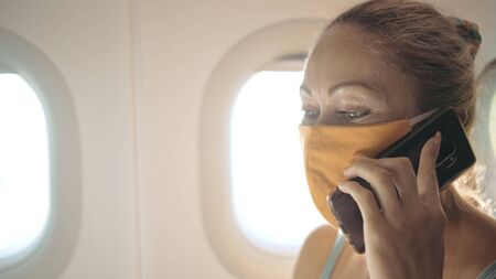 Woman travel tourist caucasian at plane aircraft with wearing protective medical mask. Girl talking about coronovirus on phone smartphone mobile. Virus epidemic sars-cov-2 covid-19 2019-ncov.の写真素材