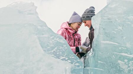 Couple has fun winter walk against background of ice of frozen lake. Lovers lie on clear ice with cracks have fun kiss and hug. View from above. Happy people on snow covered ice. Honeymoon love story.の写真素材