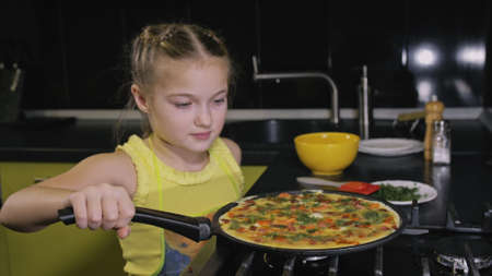 Smart girl learning to cook. Happy and serious young mistress children to cook a Neapolitan egg fried omelette from sausage. Modern Built In Kitchen Appliances in green black color.の写真素材
