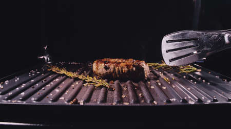 Delicious juicy meat steak cooking on grill. Kitchen tongs. Aged prime rare roast grilling...