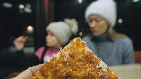 Mother and daughter eat pizza cheese four. Close up of young woman eating pizza and chewing in...