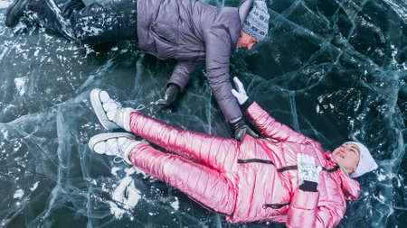 Couple has fun winter walk against background of ice of frozen lake. Lovers lie on clear ice with cracks have fun kiss and hug. View from above. Happy people on snow covered ice. Honeymoon love story.の写真素材