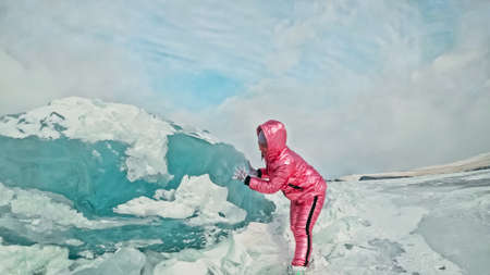Girl walking on cracked ice of frozen lake Baikal. Woman traveler explores and looks at an ice floe. Magic purest place in nature. Ice arounds traveler all his trip. Hiker walk in cosmic pink jacket.の写真素材