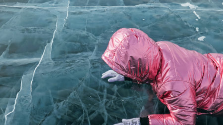 Girl walking on cracked ice of frozen lake Baikal. Woman traveler explores and looks at an ice floe. Magic purest place in nature. Ice arounds traveler all his trip. Hiker walk in cosmic pink jacket.の写真素材