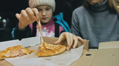 Mother and daughter eat pizza cheese four. Close up of young woman eating pizza and chewing in outdoor restaurant. Girl hands taking pieces slices of hot tasty italian pizza from open box.の写真素材
