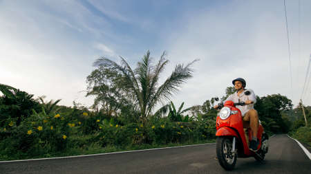 Man on red motorbike in white clothes drive on forest road trail trip. One men caucasian tourist go...