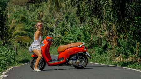 Woman on red scooter in white clothes drive on forest road trail. Dancing trip. One girl caucasian...