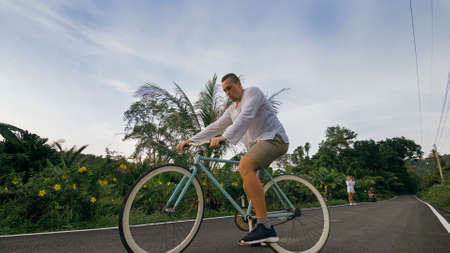 Biking road trip. The man on blue bike in white clothes on forest road. The biker men ride on bicycle. Cycling Cycle Fix. Asia Thailand ride tourism. Take a photo with a bike.の写真素材