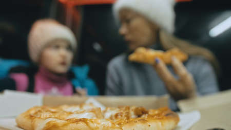 Mother and daughter eat pizza cheese four. Close up of young woman eating pizza and chewing in outdoor restaurant. Girl hands taking pieces pizza.の写真素材