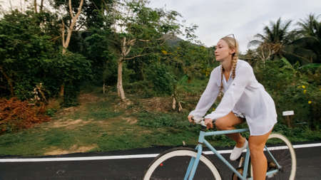 Biking road trip. The woman on blue bike in white clothes on forest road. The girl ride on bicycle. Cycling Cycle Fix. Asia Thailand ride tourism.の写真素材