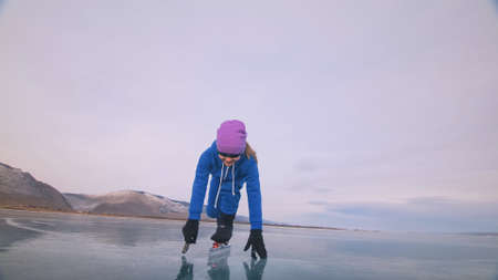 The child train on ice speed skating. The athlete at the start, in a sports stance. The kid girl skates in the winter in sportswear, sport glasses.の写真素材