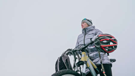 Woman stands near her bike on ice. The girl cyclist stopped to rの写真素材