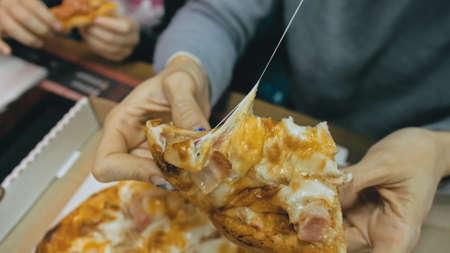Mother and daughter eat pizza cheese four. Close up of young woman eating pizza and chewing in outdoor restaurant. Girl hands taking pieces pizza.の写真素材