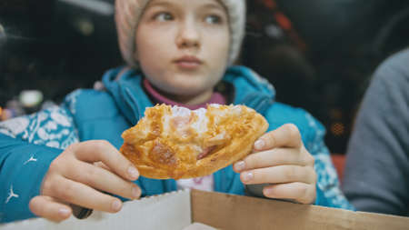 Child eat pizza cheese four. Close up of young girl woman eating pizza and chewing in outdoor restaurant. Kid children hands taking piece pizza.の写真素材