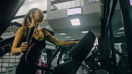 Fit Athletic Woman Exercising on an Elliptical Machine. Muscular Women Activity Training in Modern...