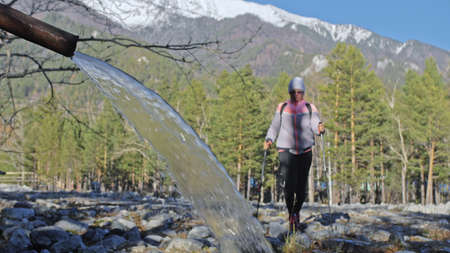 Woman do Nordic walking in nature, drinking water from a mineral source. Girls use trekking sticks and nordic poles backpacks. Family travels and goes in for sports. Autumn forest.の写真素材