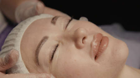 Woman receiving facial massage in spa salon on massage table. Wellness body and skin care, face beauty treatment, receiving rejuvenation procedureの写真素材