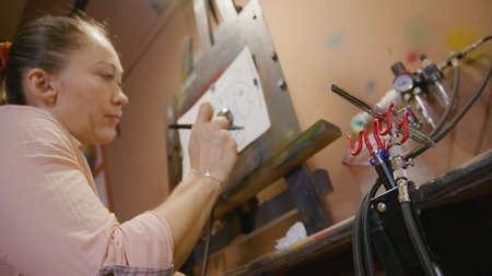 Woman artist learns to paint with airbrush with acrylic dye, paper and easel. Concept modern art,...